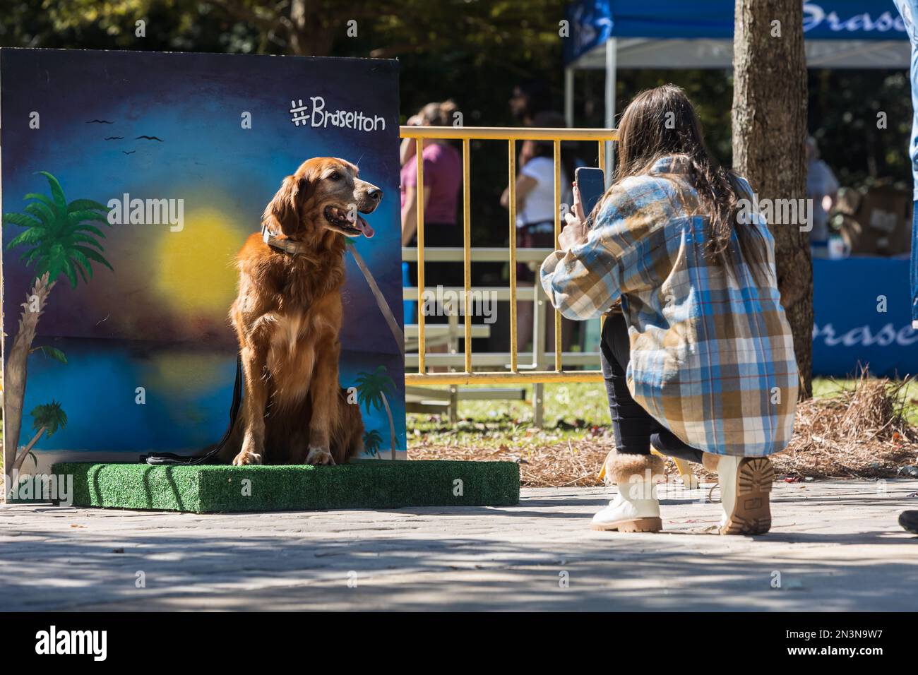 Braselton, GA / USA - 24 settembre 2022: Una donna si inginocchia per scattare una foto del suo cane seduto sullo sfondo di una foto al tramonto in un festival del cane. Foto Stock