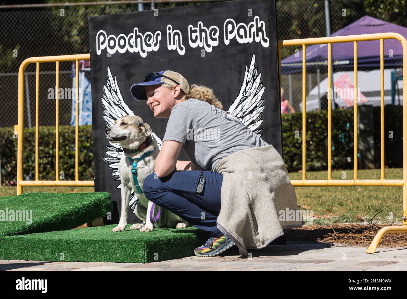Braselton, GA / USA - 24 settembre 2022: Una donna si inginocchia per scattare una foto con il suo cane seduto contro un angelo ala sfondo foto. Foto Stock
