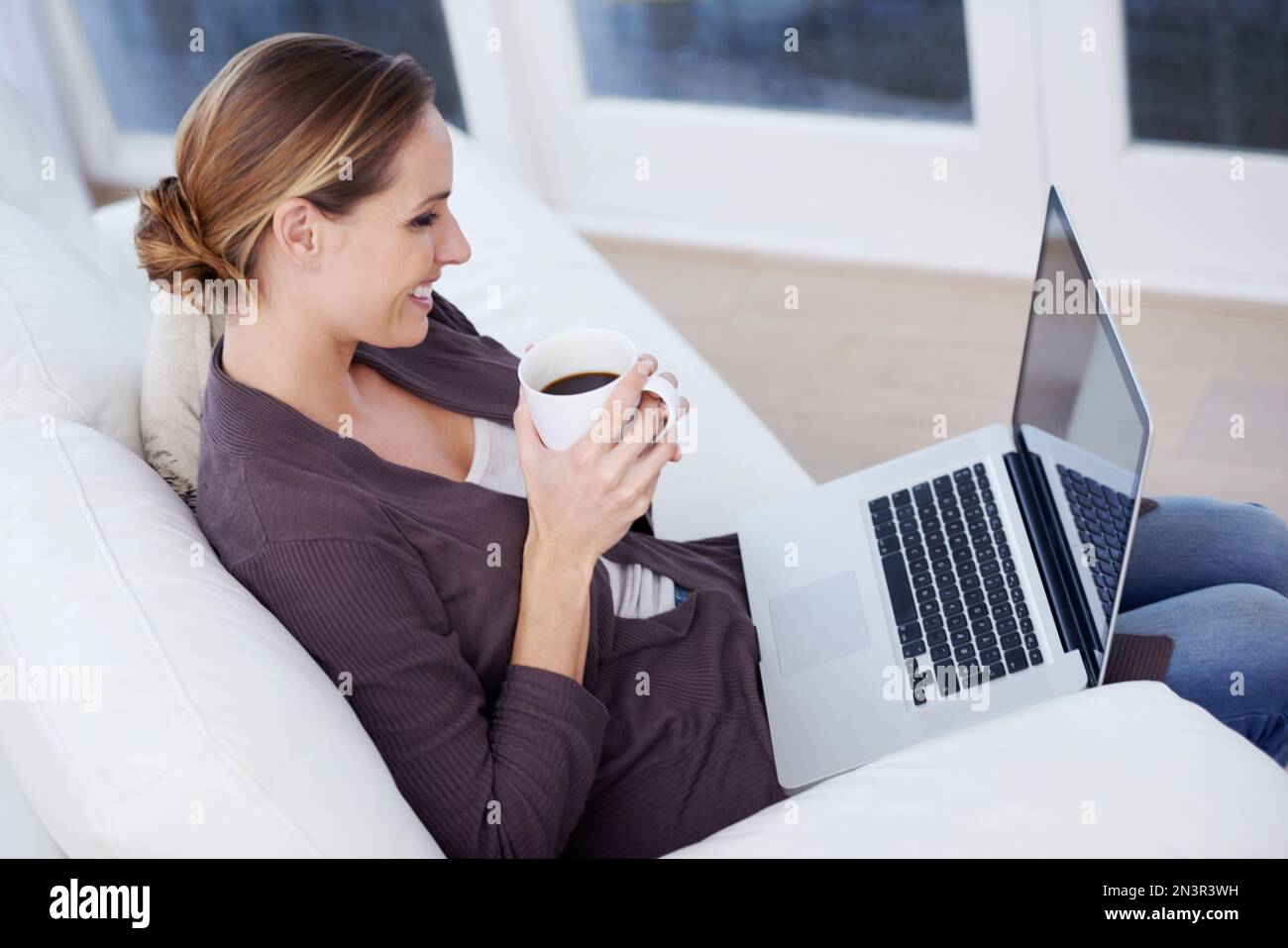 Rilassatevi con internet. Una giovane donna seduta di fronte al suo notebook con una tazza di caffè. Foto Stock