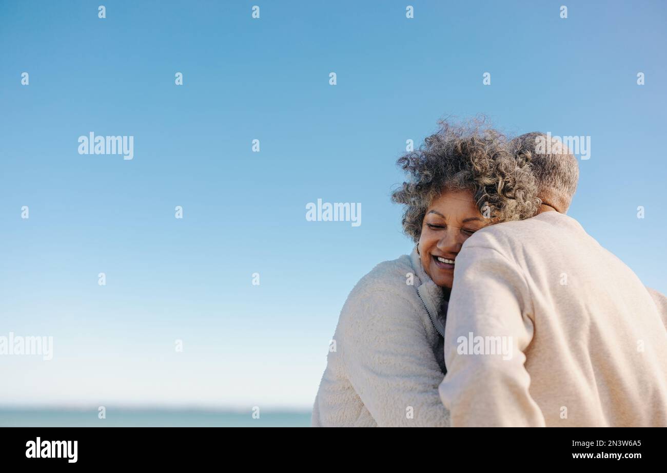 Affettuosa donna anziana sorridente felicemente mentre si appoggia alla spalla del marito in spiaggia. Romantica coppia anziana godendo di un mare rinfrescante Foto Stock