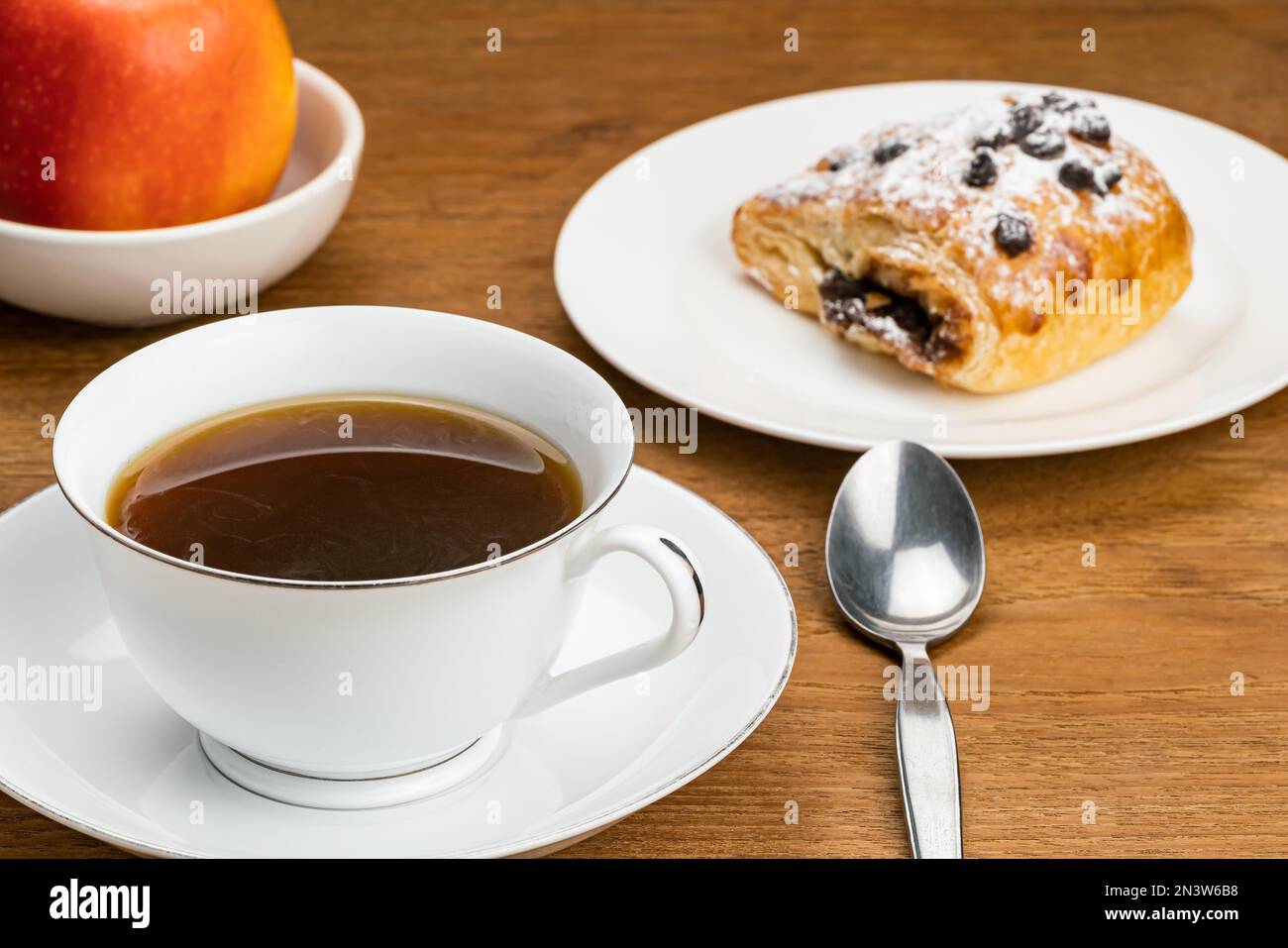 Caffè nero caldo in tazza di ceramica bianca su piattino di ceramica per colazione con pasticceria danese ripiena di crema di cioccolato con gocce di cioccolato e. Foto Stock