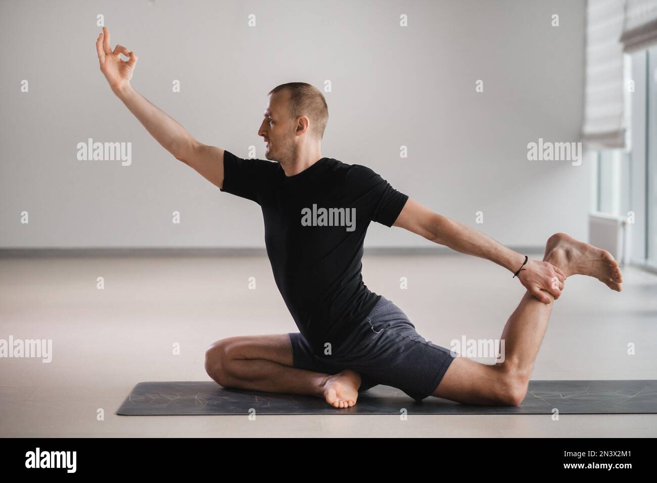 Un uomo di costruzione atletica fa yoga in palestra su un tappetino. Foto Stock