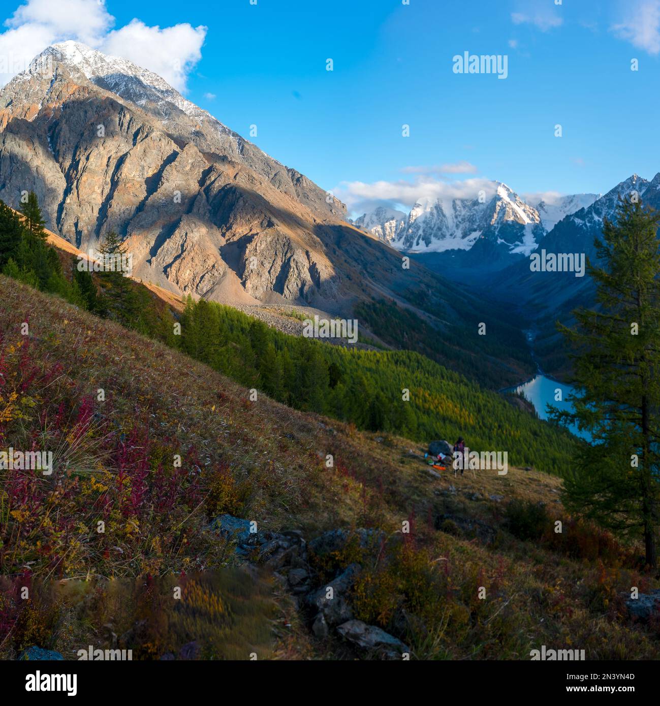 Lago alpino Shavlinskoe nella gola delle montagne all'ombra sullo sfondo dei ghiacciai con la neve in Altai con una ragazza turistica sotto di una santa Foto Stock