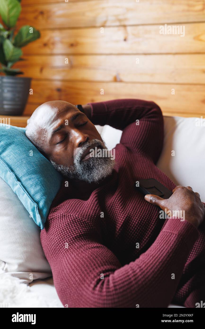 Uomo anziano calvo afro-americano con telefono cellulare che dorme sul divano in una cabina di tronchi Foto Stock