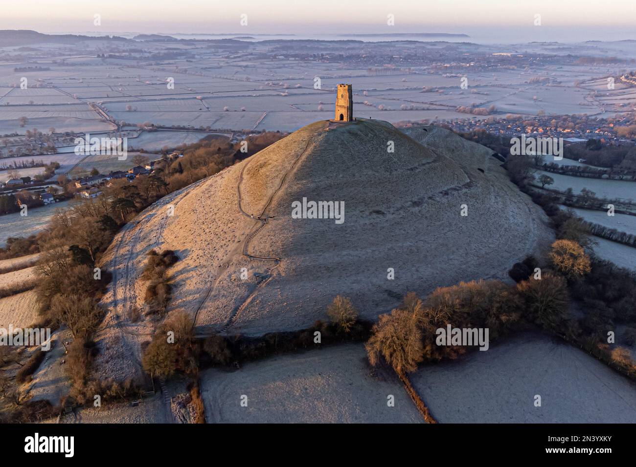 La gente sale sul ventoso sentiero verso la St Michael's Tower, in cima a Glastonbury Tor, mentre il sole sorge sopra i livelli del Somerset in una mattina fredda e croccante in molte parti del Regno Unito. Data immagine: Mercoledì 8 febbraio 2023. Foto Stock