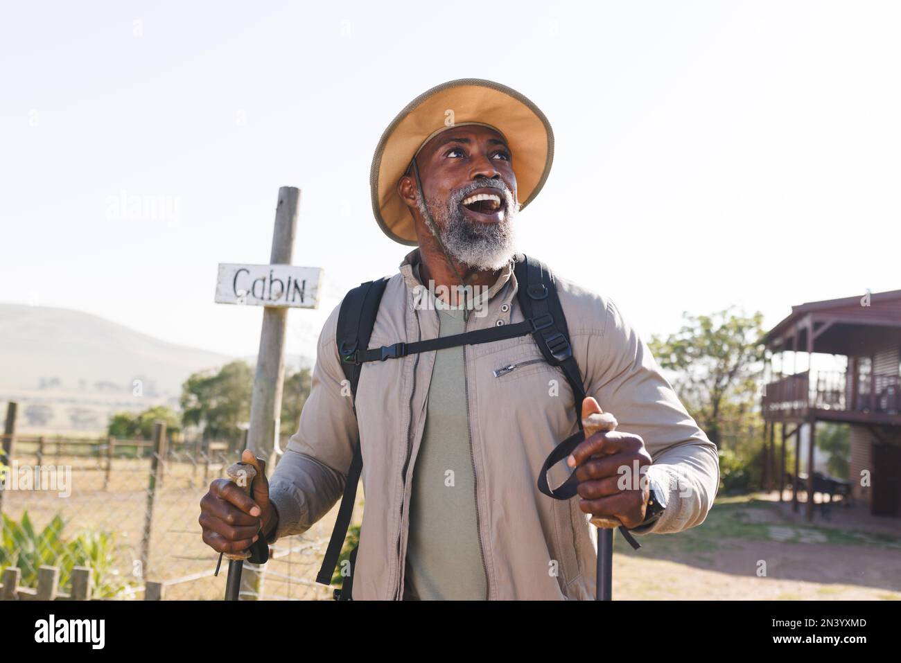 Sorpreso afroamericano uomo anziano con i pali di trekking a piedi sulla terra contro il cielo chiaro Foto Stock