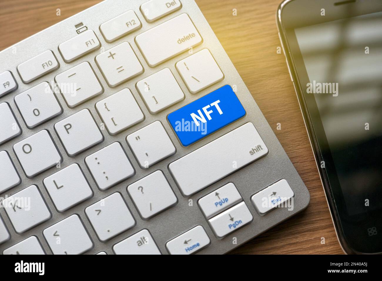 NFT o token non fungibile con tastiera e pulsante blu e un telefono cellulare sulla scrivania. Foto Stock