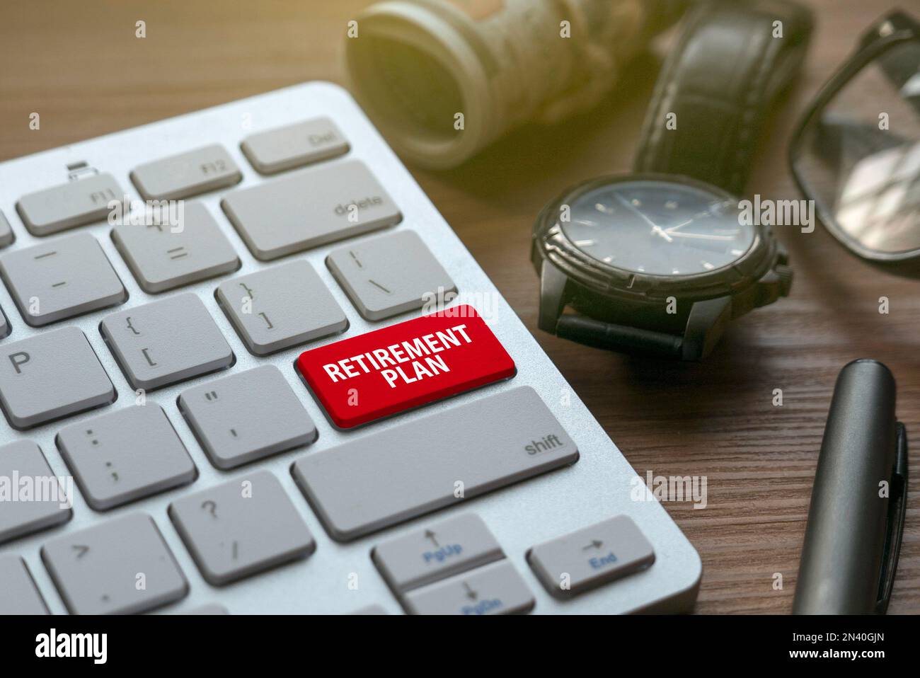 Pensionamento e pensione con denaro, orologio, occhiali, penna e tastiera con pulsante rosso scritto con piano di pensionamento. Foto Stock