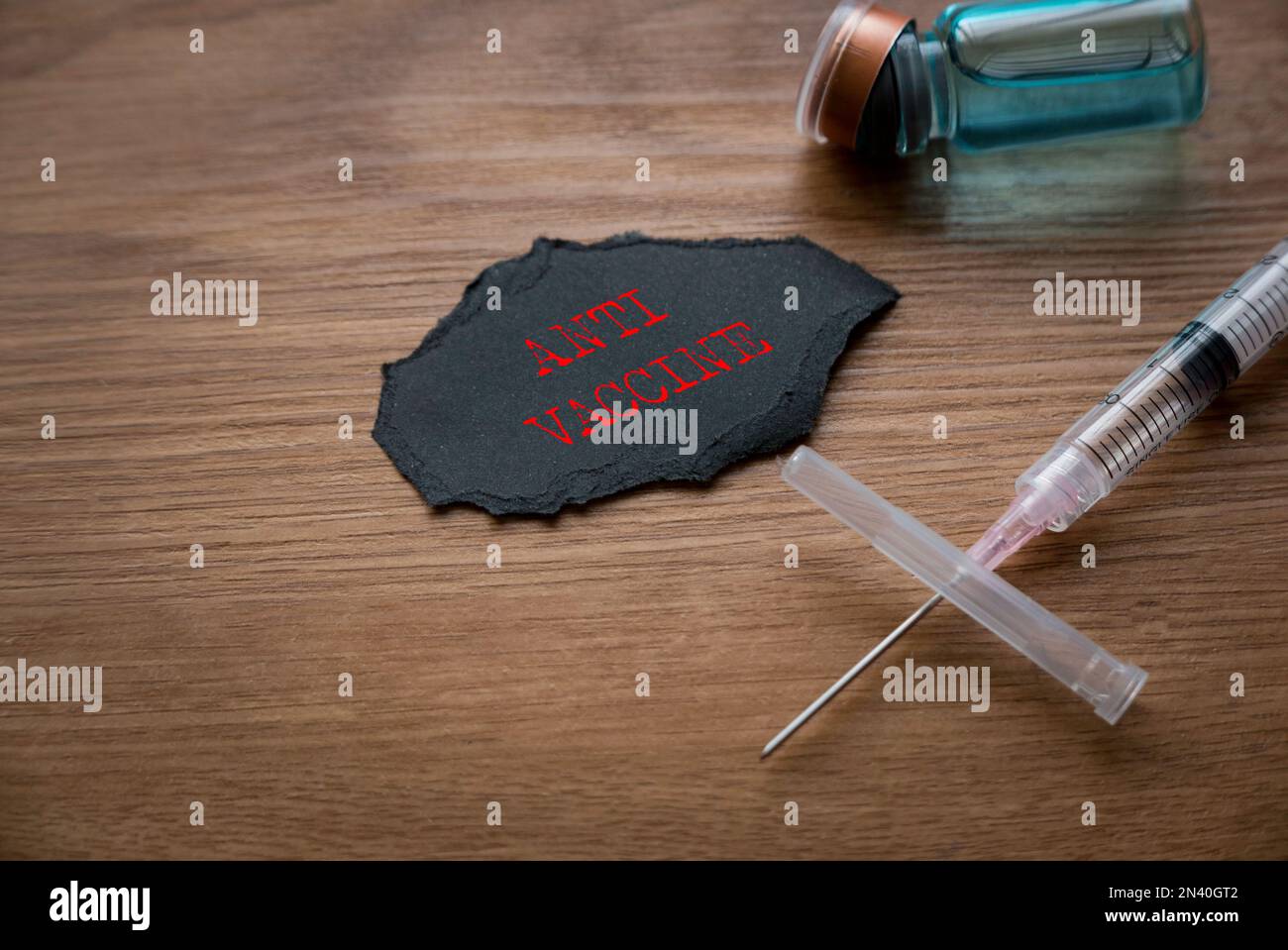 Una bottiglia di vaccino, una siringa e un pezzo di carta nera scritta con Anti Vaccine su sfondo di legno. Foto Stock