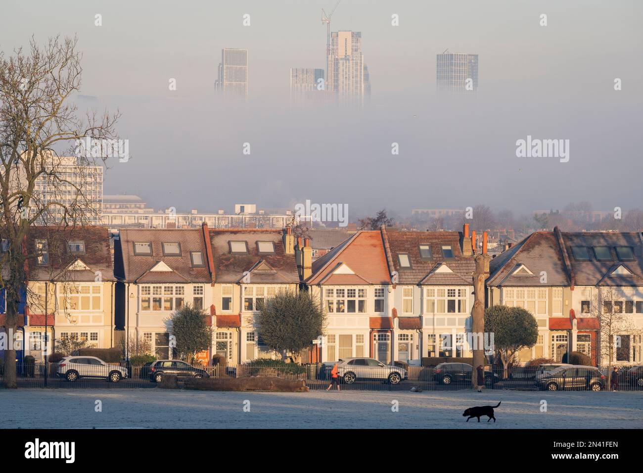 Un corridore passa davanti alle case edoardiane che confinano con Ruskin Park e la nebbia mattutina oscura parzialmente gli alti edifici residenziali in lontananza a nove Foto Stock