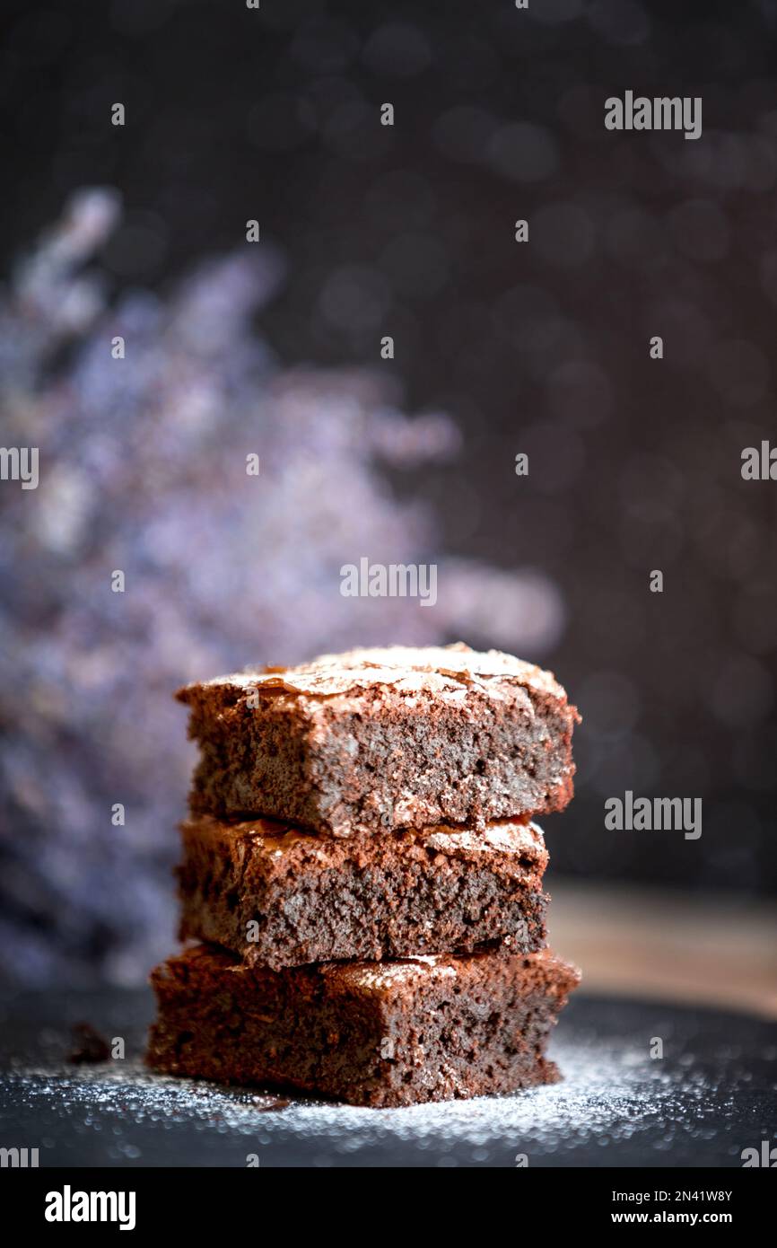 Torta di brownie al cioccolato fondente fatta in casa impilata su un piatto di pietra con spazio per le copie. Fiori di lavanda sfondo Foto Stock