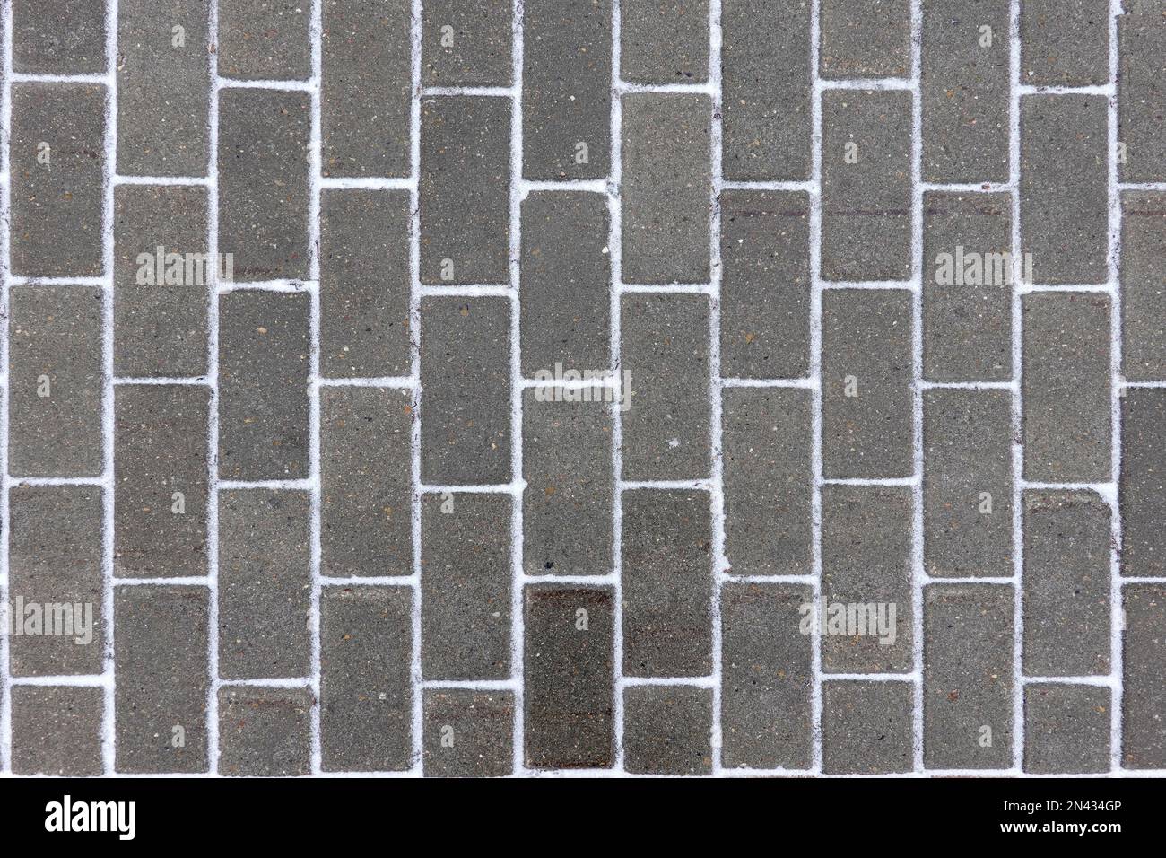 Lastre di pavimentazione grigio scuro come sfondo con stripes di neve tra i blocchi vista dall'alto in primo piano Foto Stock
