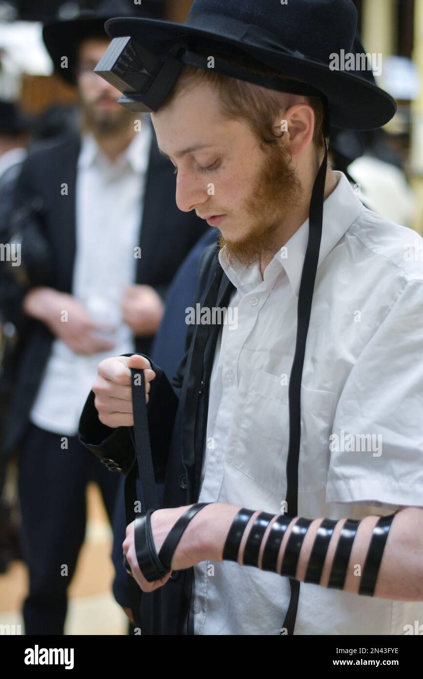 Un giovane manichetta hassidica sul suo tefillin al servizio di preghiera mattutino nella sinagoga principale di Lubavitch sulla Eastern Parkway a Brooklyn, New York. Foto Stock
