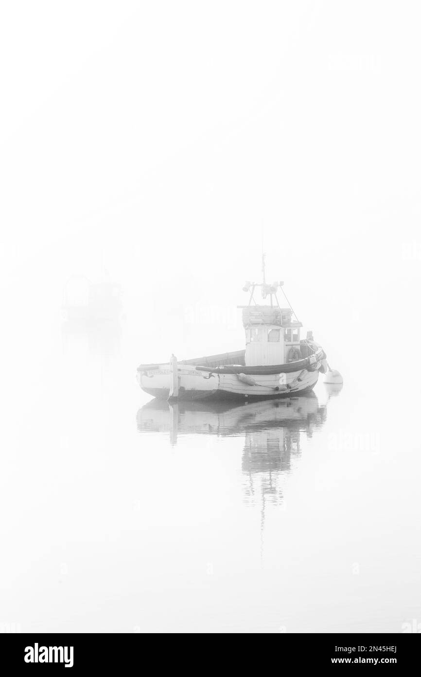 Barche ormeggiate sul fiume ore al largo di Orford Quay a Suffolk in una fredda mattina di febbraio come nebbia & nebbia inizio a Clear. Un'immagine monocromatica astratta Foto Stock