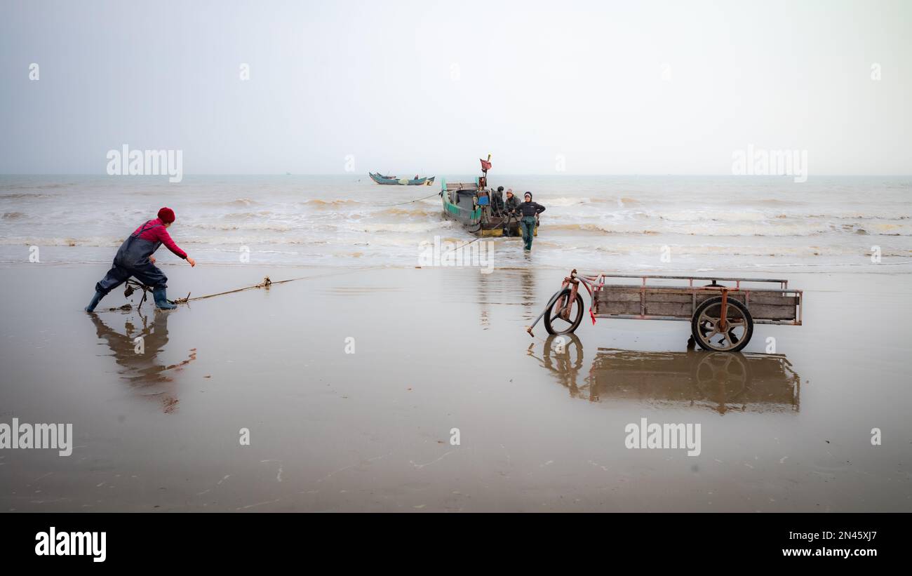 Una donna di pesca lotta per pesare l'ancora come si prepara a partire per pescare dalla spiaggia di tra Co, vicino a Mong Cai, a Quang Ninh, Vietnam Foto Stock