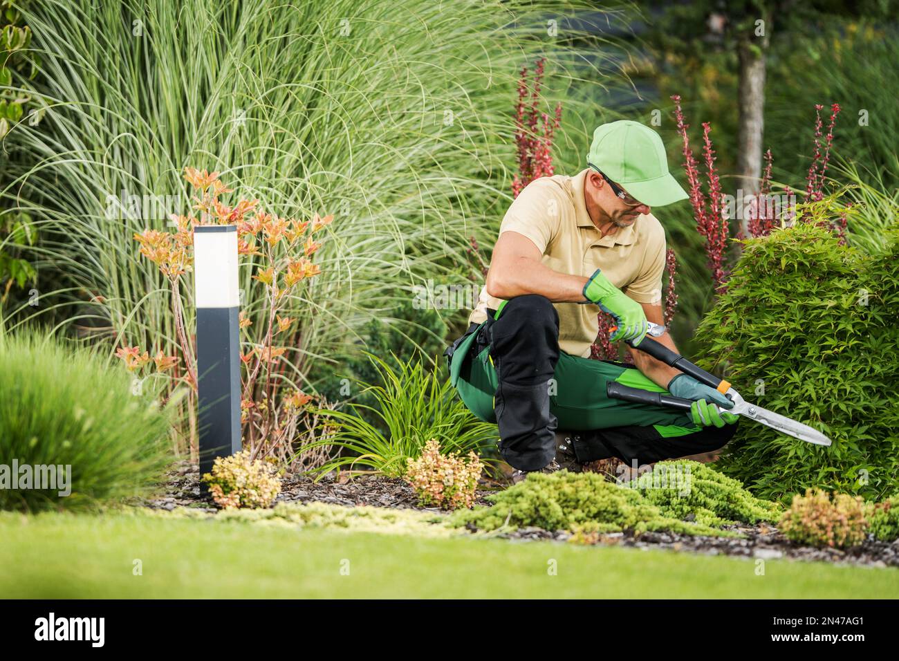 Giardiniere professionista con grandi forbici all'interno di un bellissimo giardino maturo. Giardinaggio e architettura del paesaggio tema di industria. Foto Stock