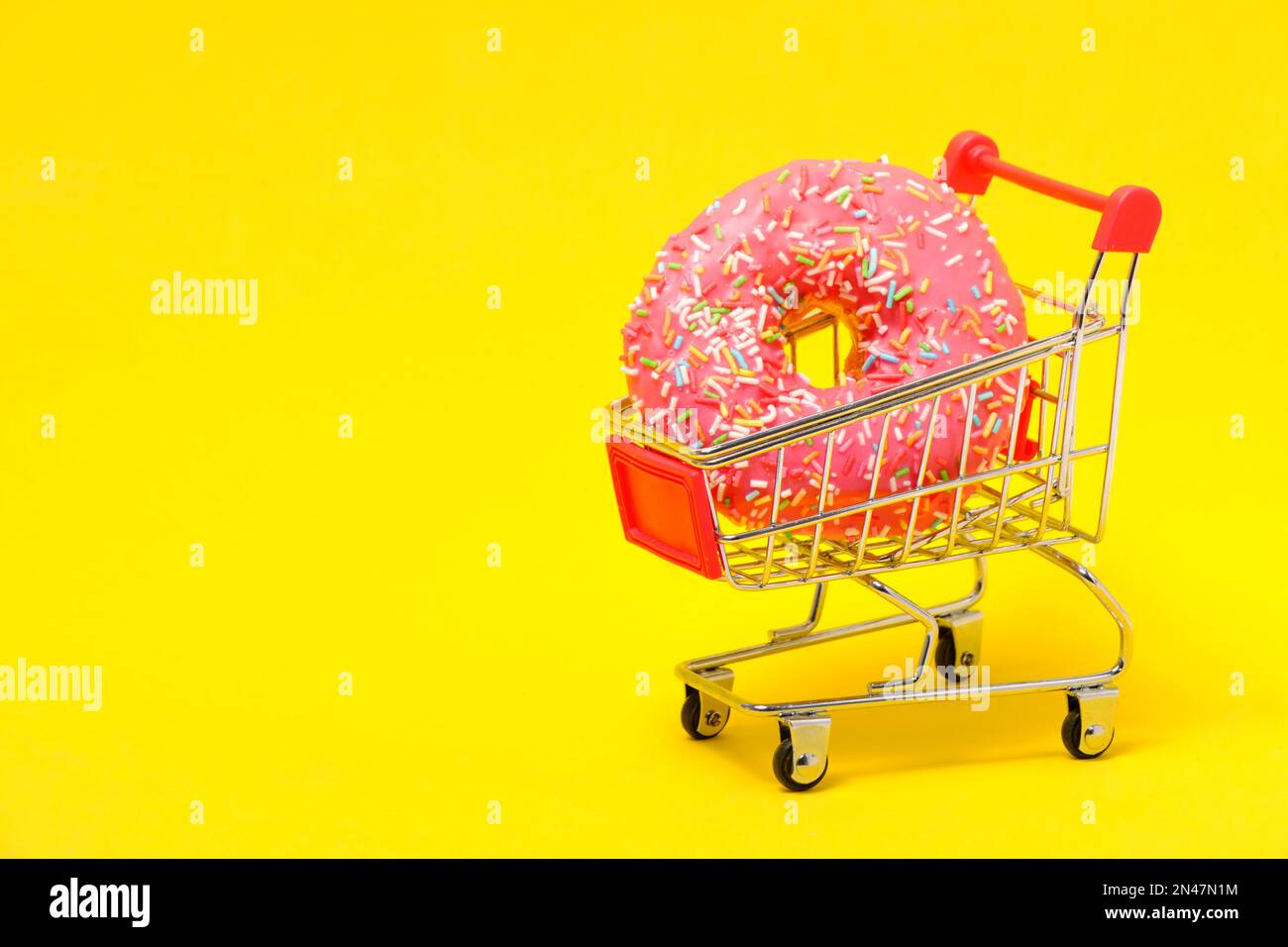 Ciambella con glassa rosa e zucchero multicolore cosparsa nel carrello della spesa su sfondo giallo Foto Stock