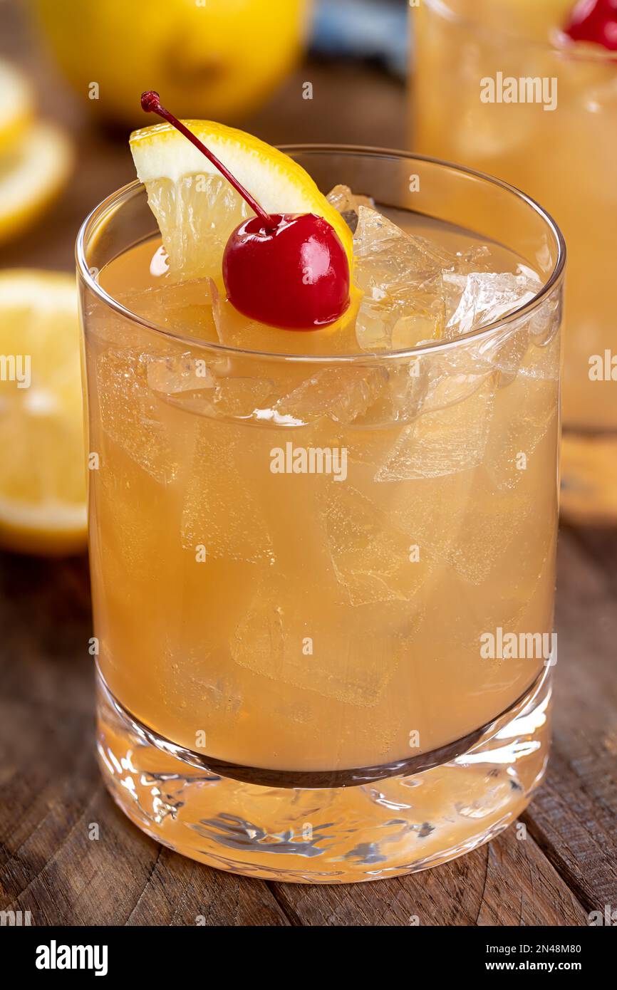 Cocktail acido di whiskey con ciliegia di marachino e fetta di limone su un rustico tavolo di legno. Vista in primo piano Foto Stock