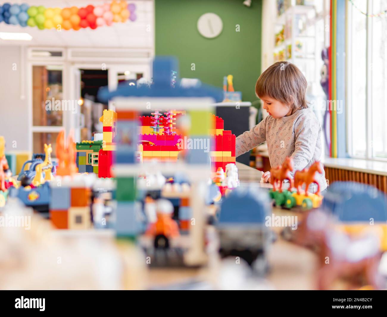 Il bambino gioca con i blocchi colorati del giocattolo. Il bambino fissa la figura dal costruttore del giocattolo. Interno dell'asilo o della scuola materna. Foto Stock