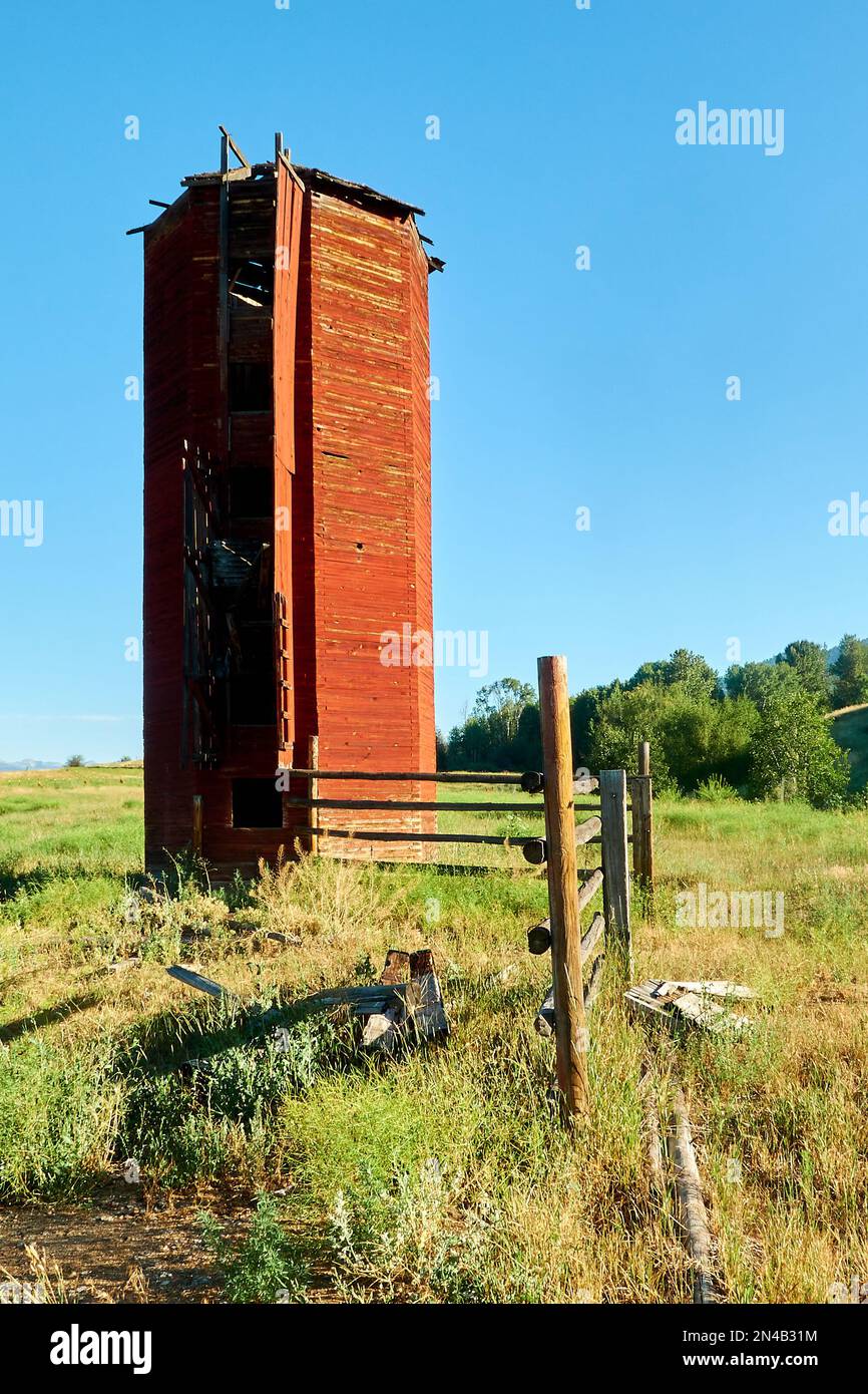 Vecchio silo rosso accanto a una recinzione in una fattoria in un campo di erba verde Foto Stock