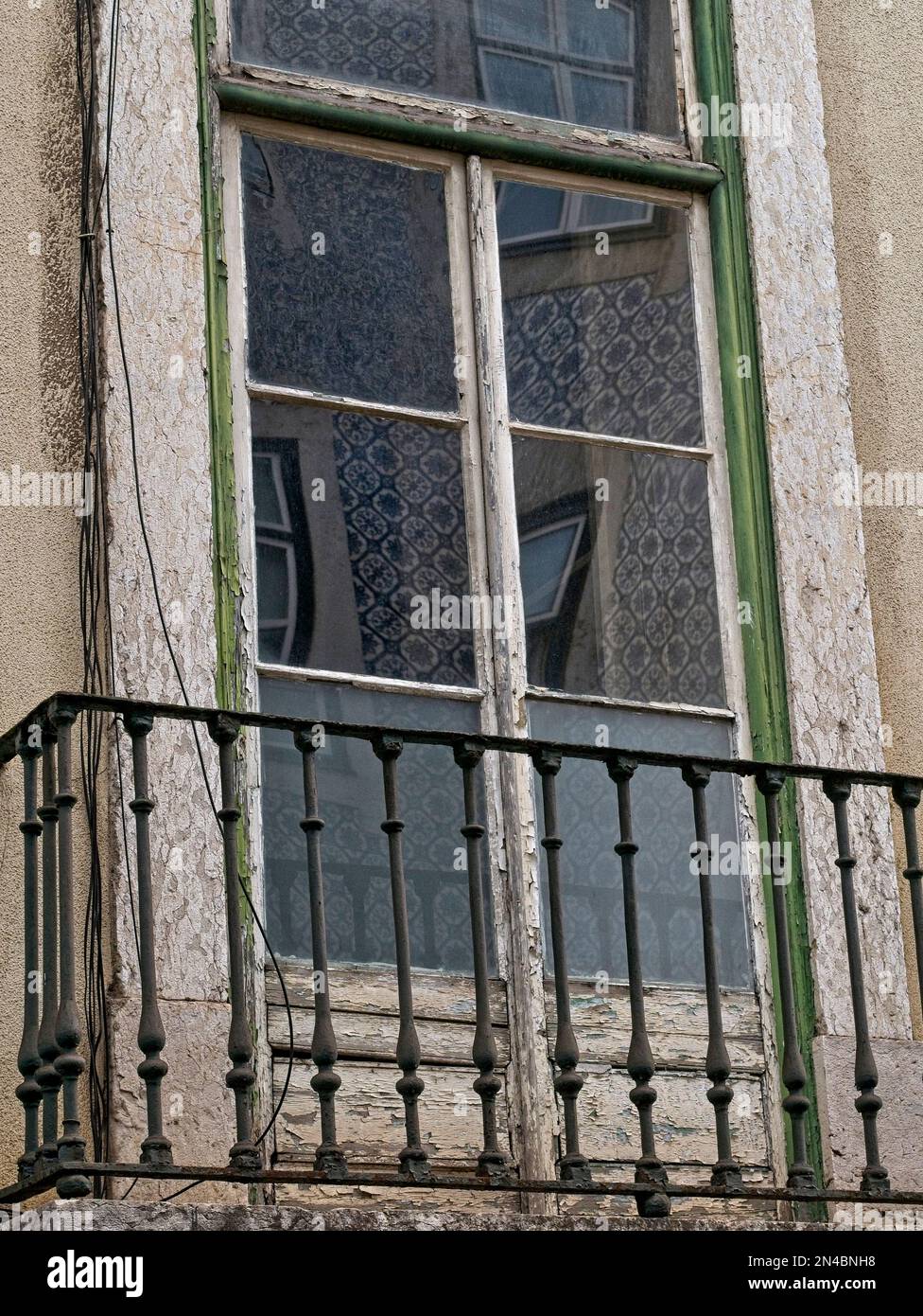 Vecchia finestra fatiscente e intaccata a Lisbona, Portogallo, con vernice da peeling, sporcizia, sporcizia, un balcone e una finestra che riflette un edificio piastrellato Foto Stock