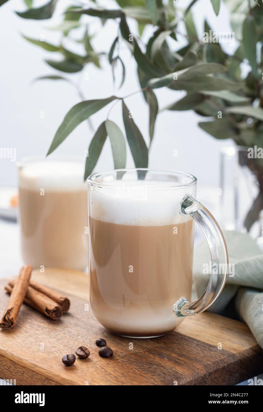 Due cappuccino o latte con schiuma di latte in bicchieri su un piatto di legno con chicchi di caffè, cannella ed eucalipto ramificano da vicino. Il concetto di primavera Foto Stock