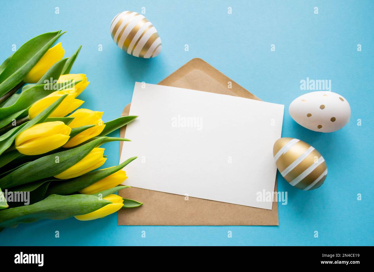 Auguri di Pasqua: Tulipani gialli, uova dorate e bianche su sfondo blu. Una lettera con spazio per la copia. Vacanze di primavera. Foto Stock