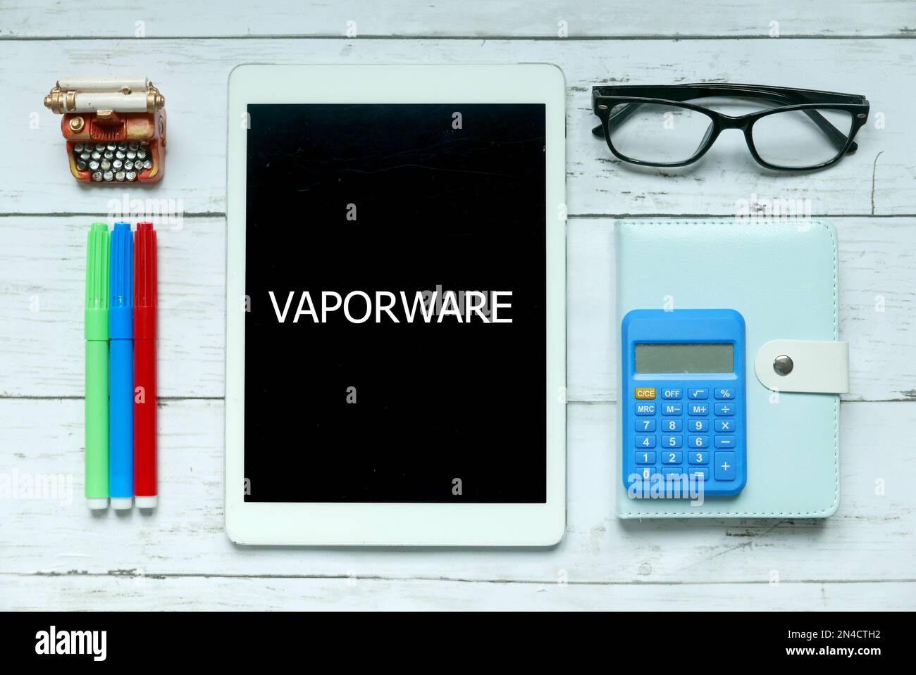 Concetto aziendale. Vista dall'alto di penna colorata, calcolatrice, occhiali, penna, notebook e tablet scritti con Vaporware su sfondo di legno bianco. Foto Stock
