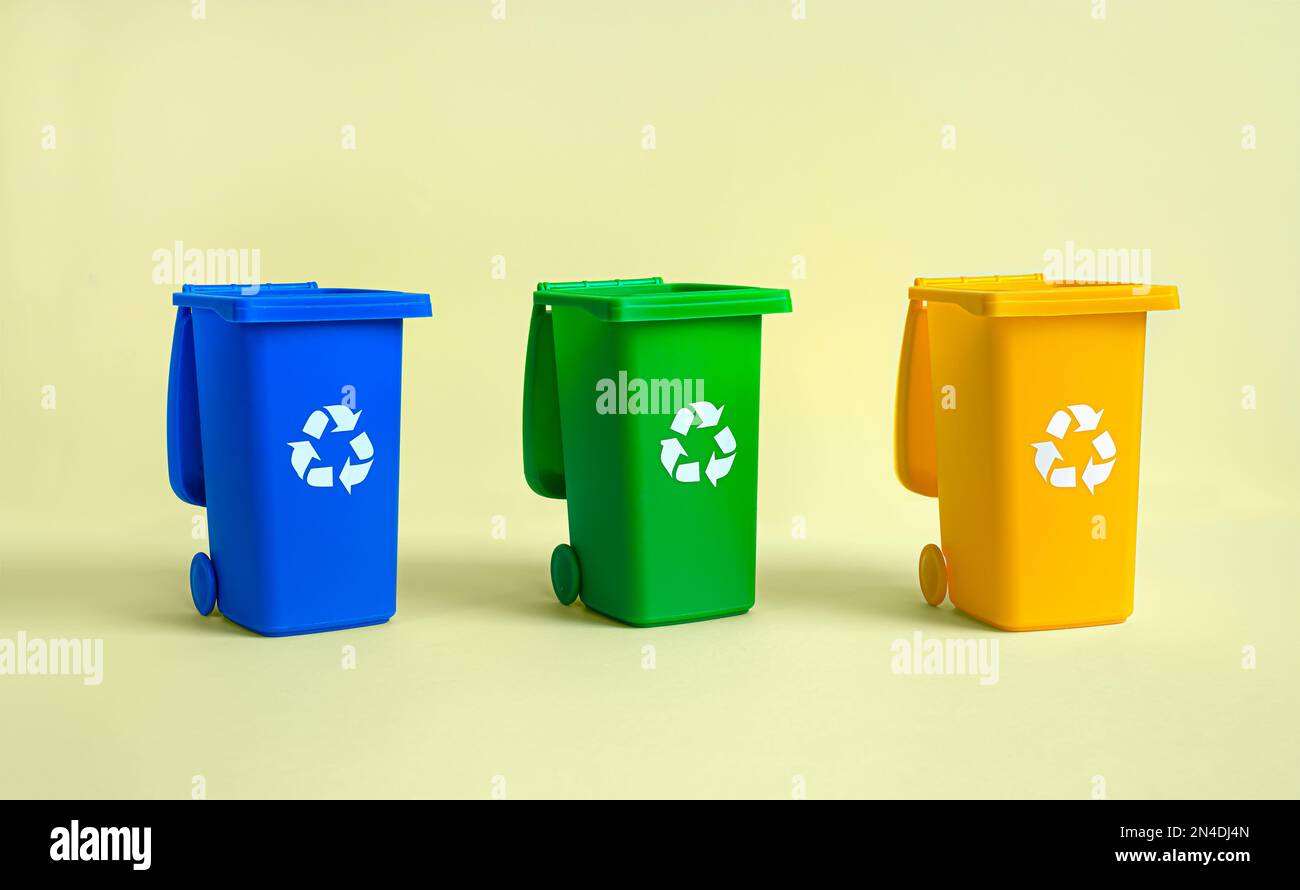 Serbatoio blu, giallo e verde per la raccolta differenziata dei rifiuti su sfondo giallo, riciclaggio dei rifiuti e conservazione dell'ambiente Foto Stock