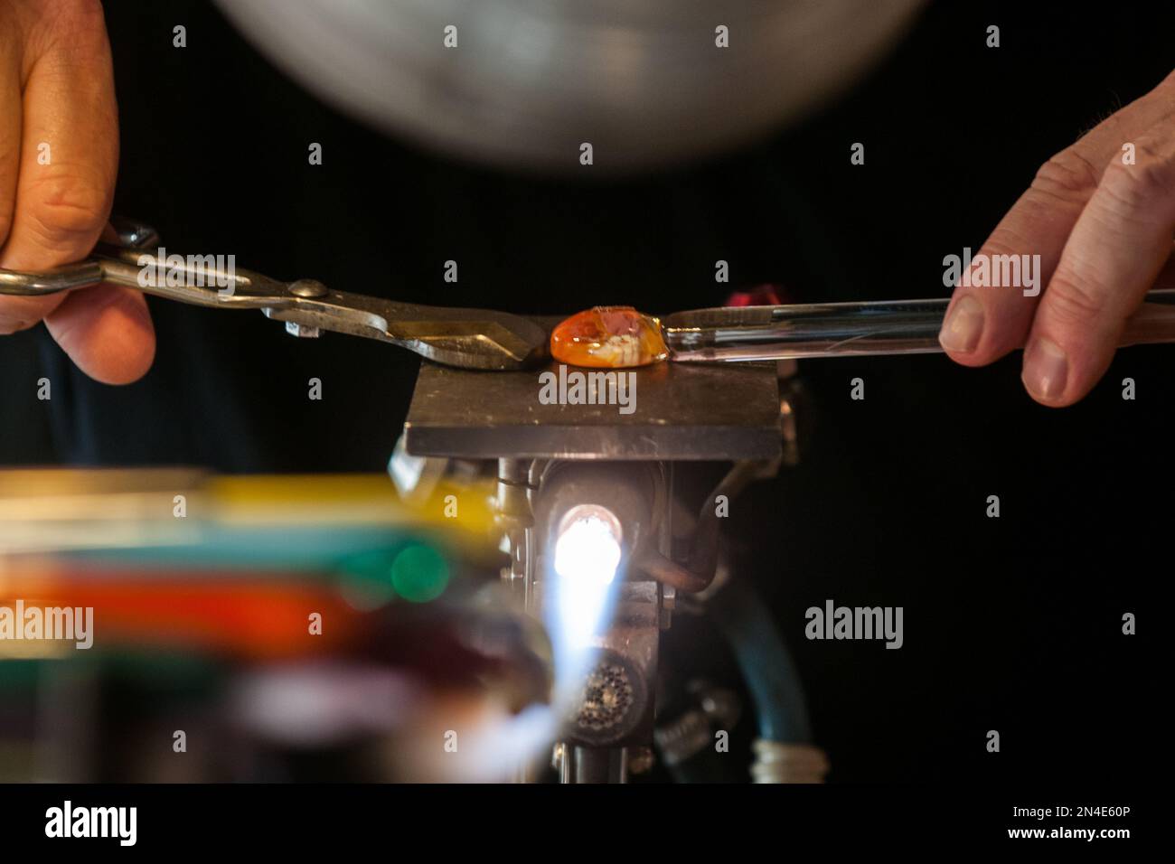 Un maestro artigiano che forma un vetro luminoso in un'area di lavoro Foto Stock