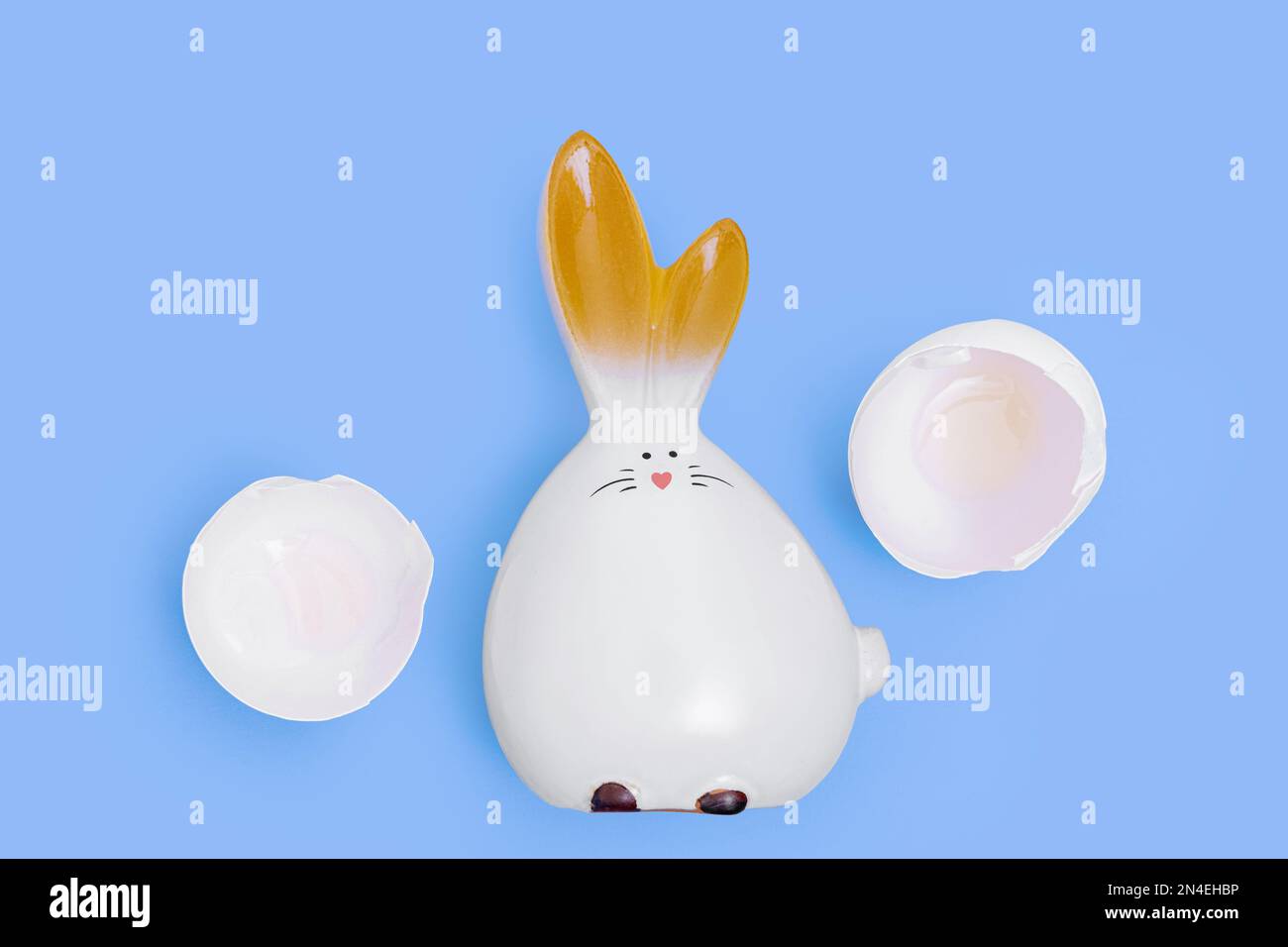 Un coniglietto pasquale bianco tratteggiato e gusci di uovo rotti su uno sfondo blu. Pasqua minima composizione creativa. Buona vacanza di Pasqua. Un biglietto d'auguri. Foto Stock