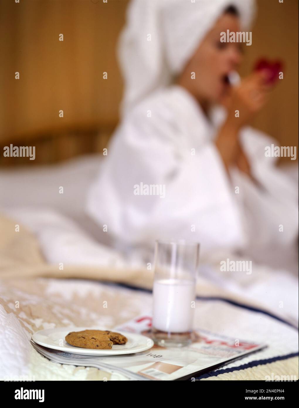 Giovane donna adulta in accappatoio vestendo Lipstick in camera d'albergo, latte e biscotti in primo piano Foto Stock