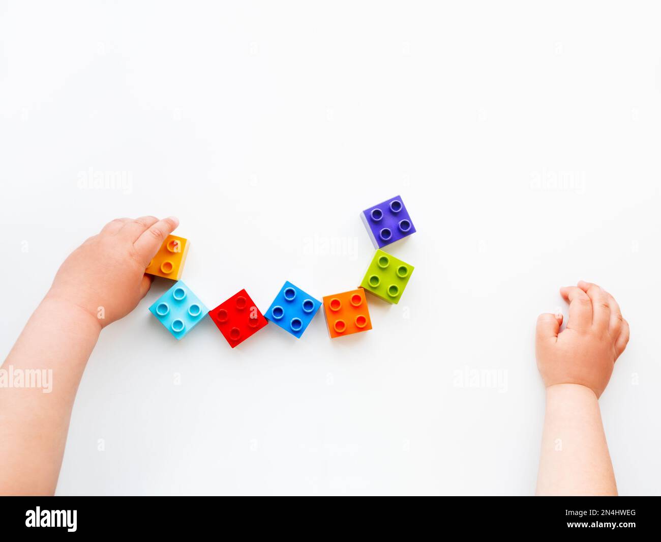 Il bambino sta giocando con i blocchi costruttori colorati. Le mani del bambino con il giocattolo dei mattoni su fondo bianco. Giocattolo didattico, piatto, vista dall'alto. Foto Stock