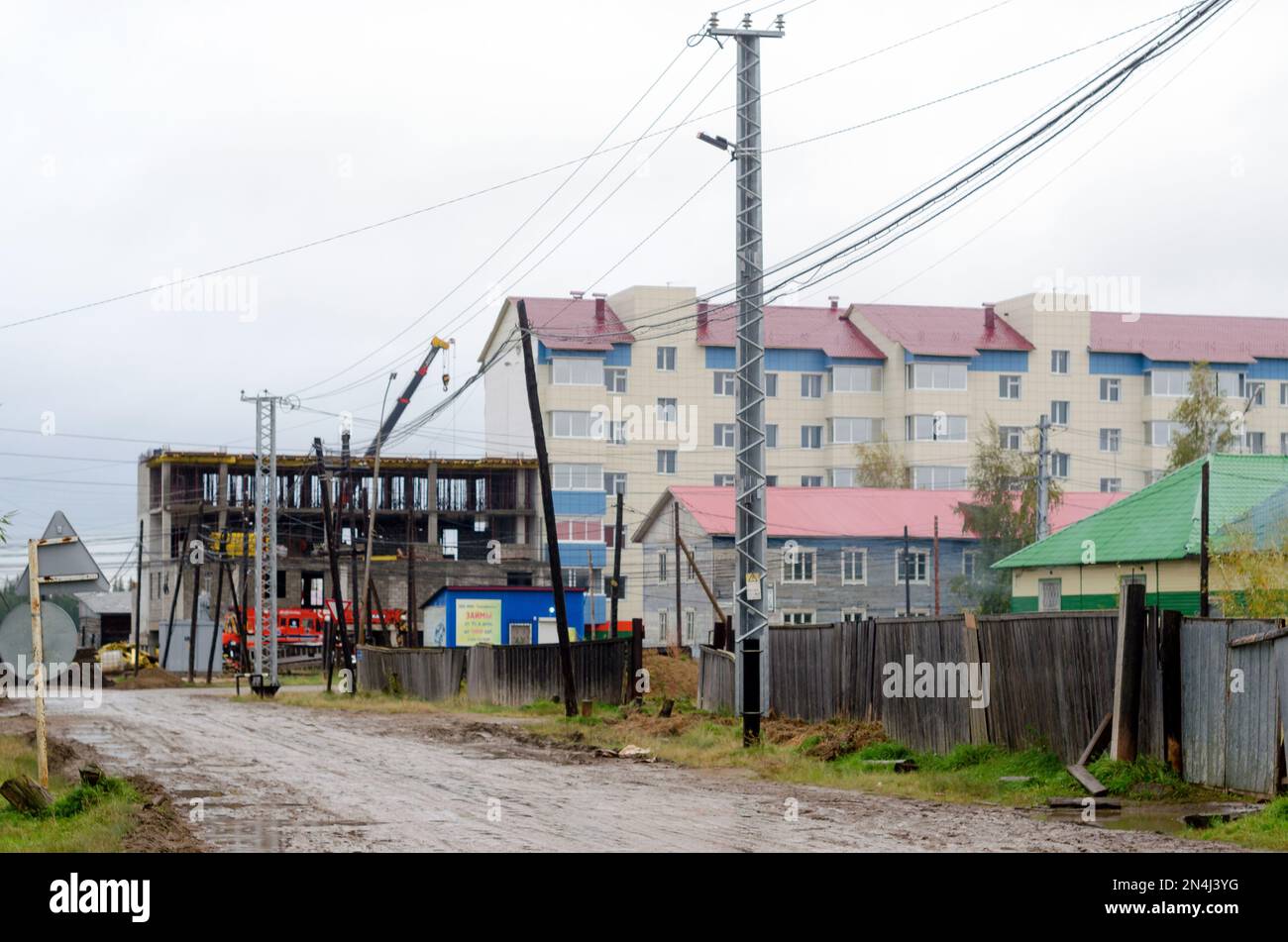 La costruzione di un nuovo edificio a più piani nel nord nel villaggio di Yakutia, suntar alla fine della strada bagnata con una recinzione di vecchia ferrovia Foto Stock