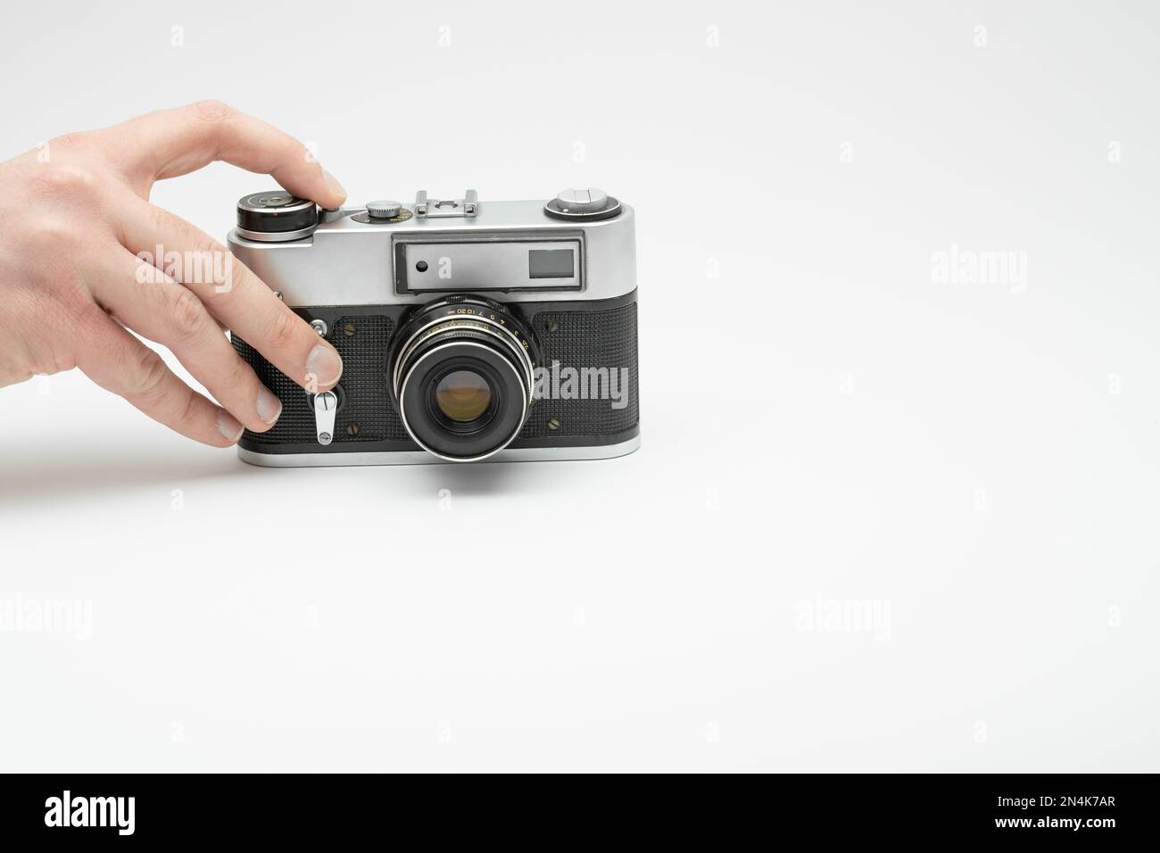 Mano premendo il pulsante di scatto su una telecamera d'epoca isolata sul backgorund bianco. Scattare foto a mano con una vecchia telecamera. Premere con il dito il Foto Stock