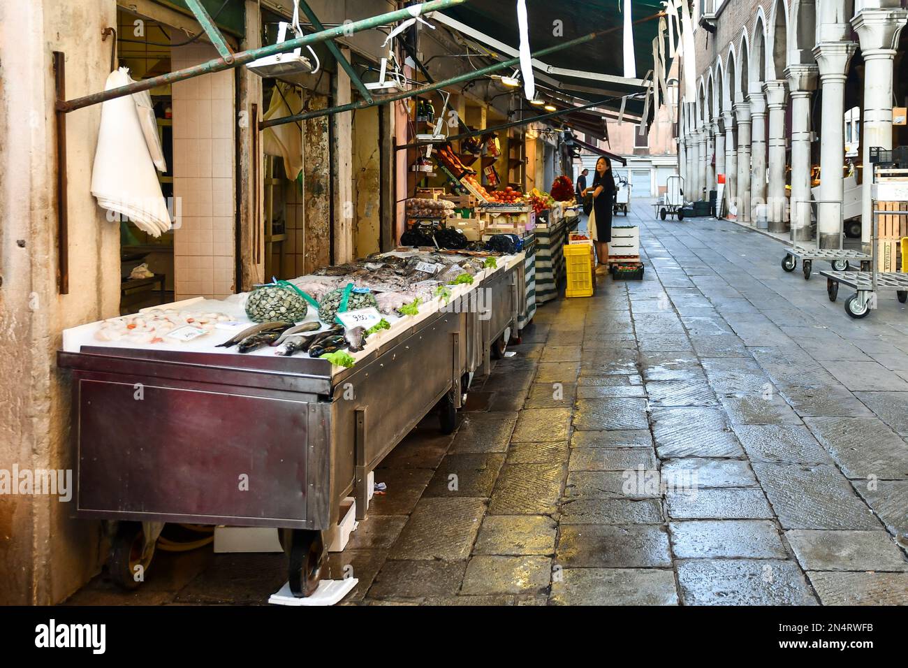 Un negozio di pesce con il pescato del giorno esposto sul marciapiede e un negozio di alimentari di fronte alla Loggia del mercato del pesce, San Polo, Venezia, Italia Foto Stock