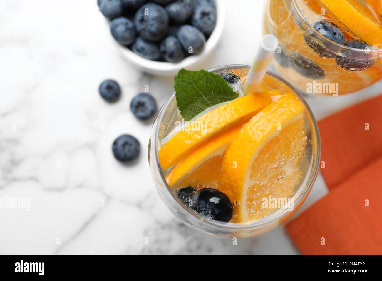 Piatto posa composizione di deliziosa limonata d'arancia con acqua sodica, menta e mirtilli su tavola di marmo bianco. Cocktail estivo fresco Foto Stock