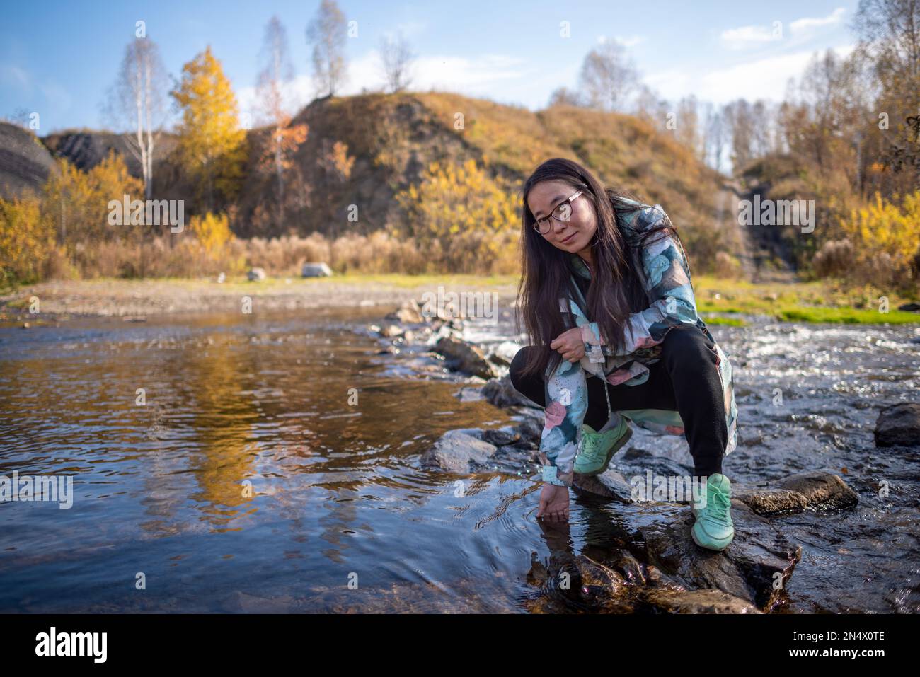 Yakut ragazza asiatica in occhiali in posa sorridente seduto accanto all'acqua e toccare la superficie. Foto Stock
