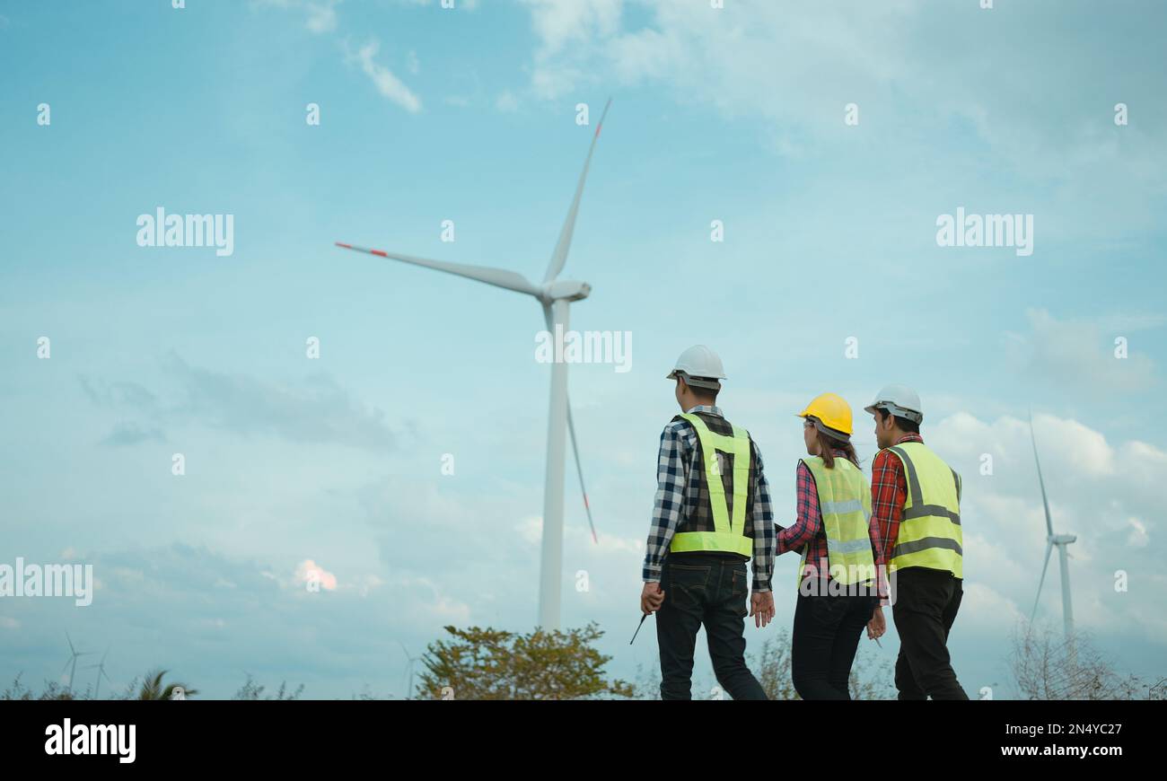 Vista posteriore di tre ingegneri che discutono e controllano lo stato di avanzamento del campo delle turbine eoliche. Foto Stock
