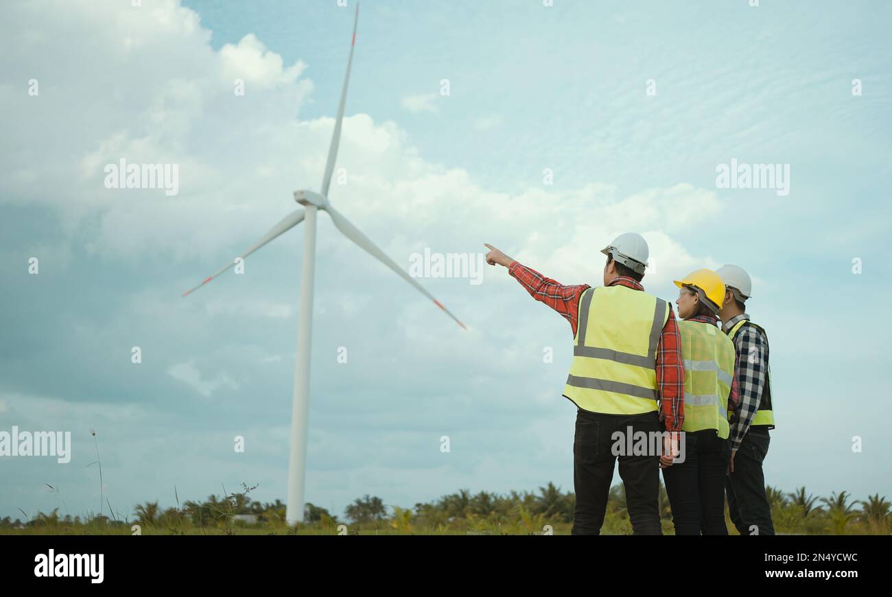 Vista posteriore di tre ingegneri che discutono e controllano lo stato di avanzamento del campo delle turbine eoliche. Foto Stock