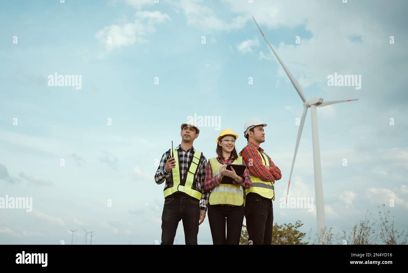Ritratto di un gruppo di ingegneri felici che guardano in un campo agricolo con turbine eoliche. Concetto di energia pulita e rinnovabile. Foto Stock