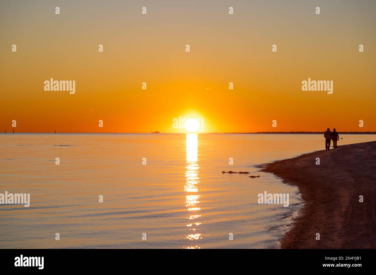 Mano nella mano, una coppia ha camminato lungo il litorale, bagnato nelle tonalità calde e dorate del sole di regolazione, generando un momento da quadro-perfetto di romanticismo. Foto Stock