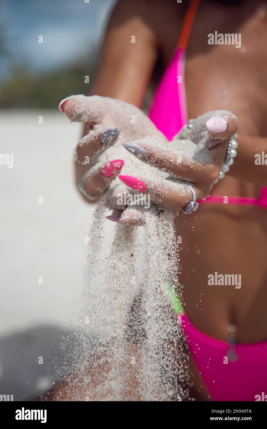 Sabbia che scivola attraverso le dita di una mano di donna che indossa un bikini rosa Foto Stock