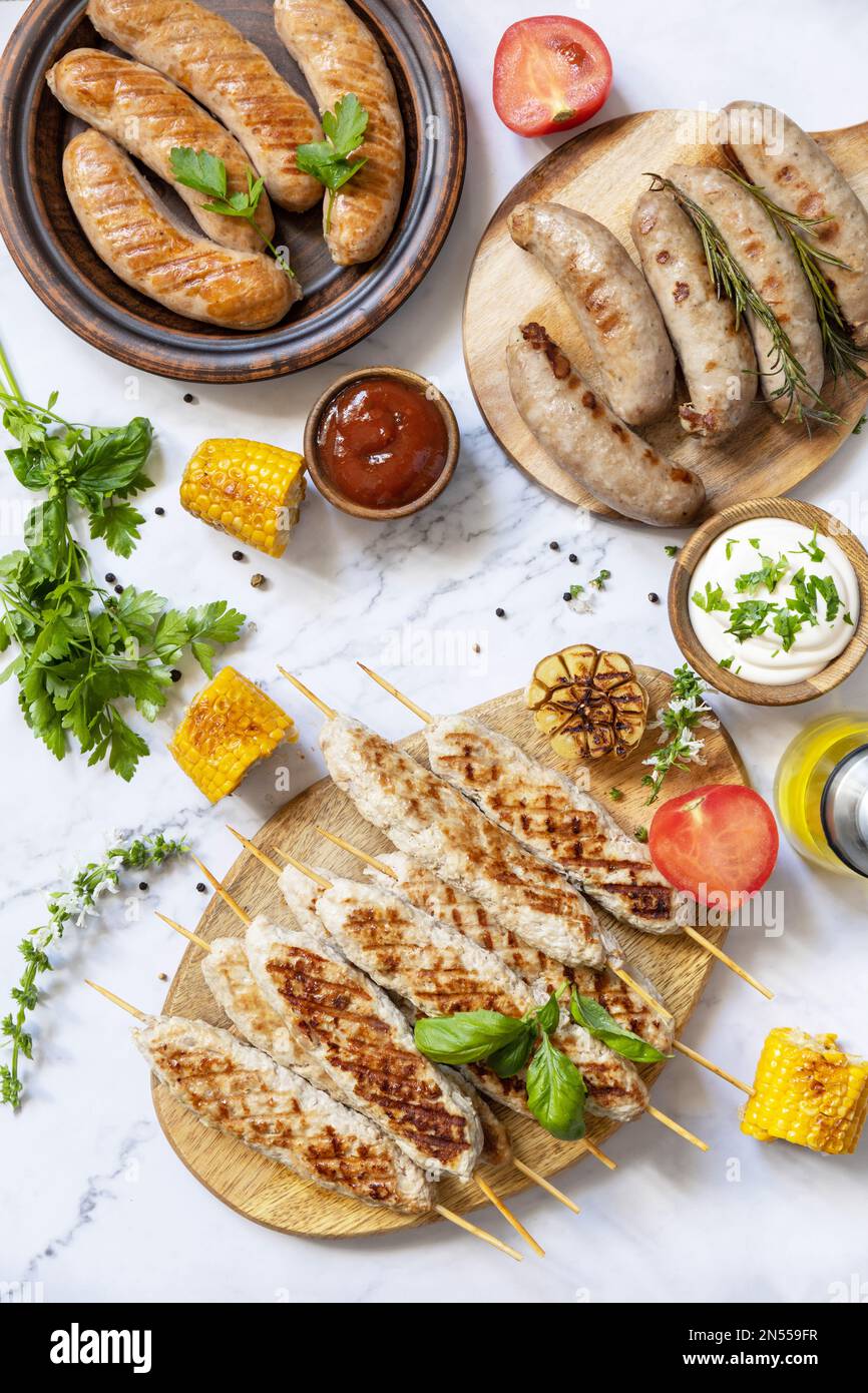 Menu di piatti alla griglia. Varie salsicce alla griglia con erbe fresche e spezie su un tavolo in marmo. Estate festa cibo. Foto Stock