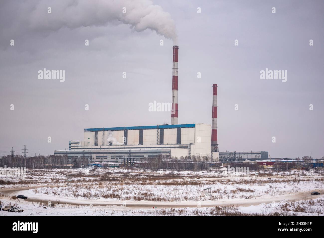La strada con le derive da neve e le auto veloci va contro lo sfondo di grandi caldaie di una potente centrale termica sul fumo di carbone nel cielo in t Foto Stock