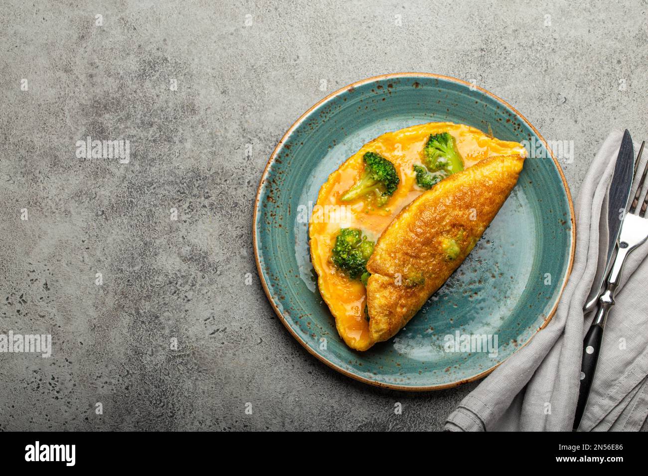 Sana frittata vegetariana con broccoli verdi ripiegati a metà serviti su piatto con vista dall'alto a forchetta e coltello, fondo in cemento di pietra grigia Foto Stock