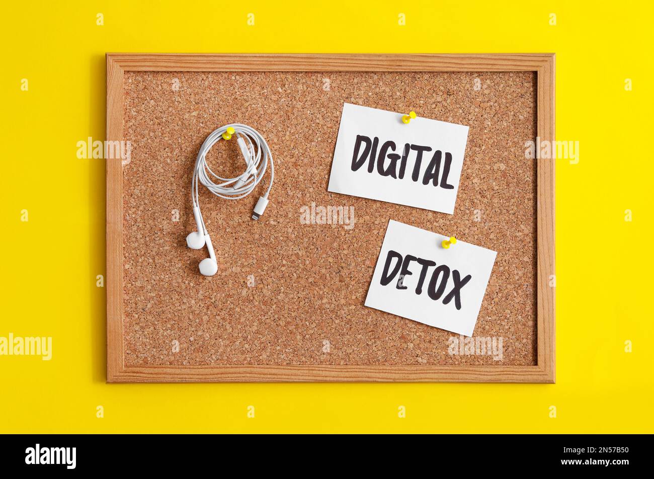 Corkboard con parole DETOX DIGITALE e auricolari appesi su sfondo giallo Foto Stock