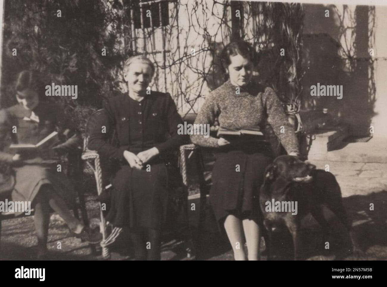 Fotografia vintage sui cani da compagnia : cucciolo con mano. Giovani donne (sorelle o fidanzate BFFs ( migliori amici per sempre )) e loro madre o nonna con un super felice e super sorridente grande cane nero in posa per la macchina fotografica. questo cane è super star. è super carino, felice e sorridente. la foto è stata scattata al 1930s. Foto Stock