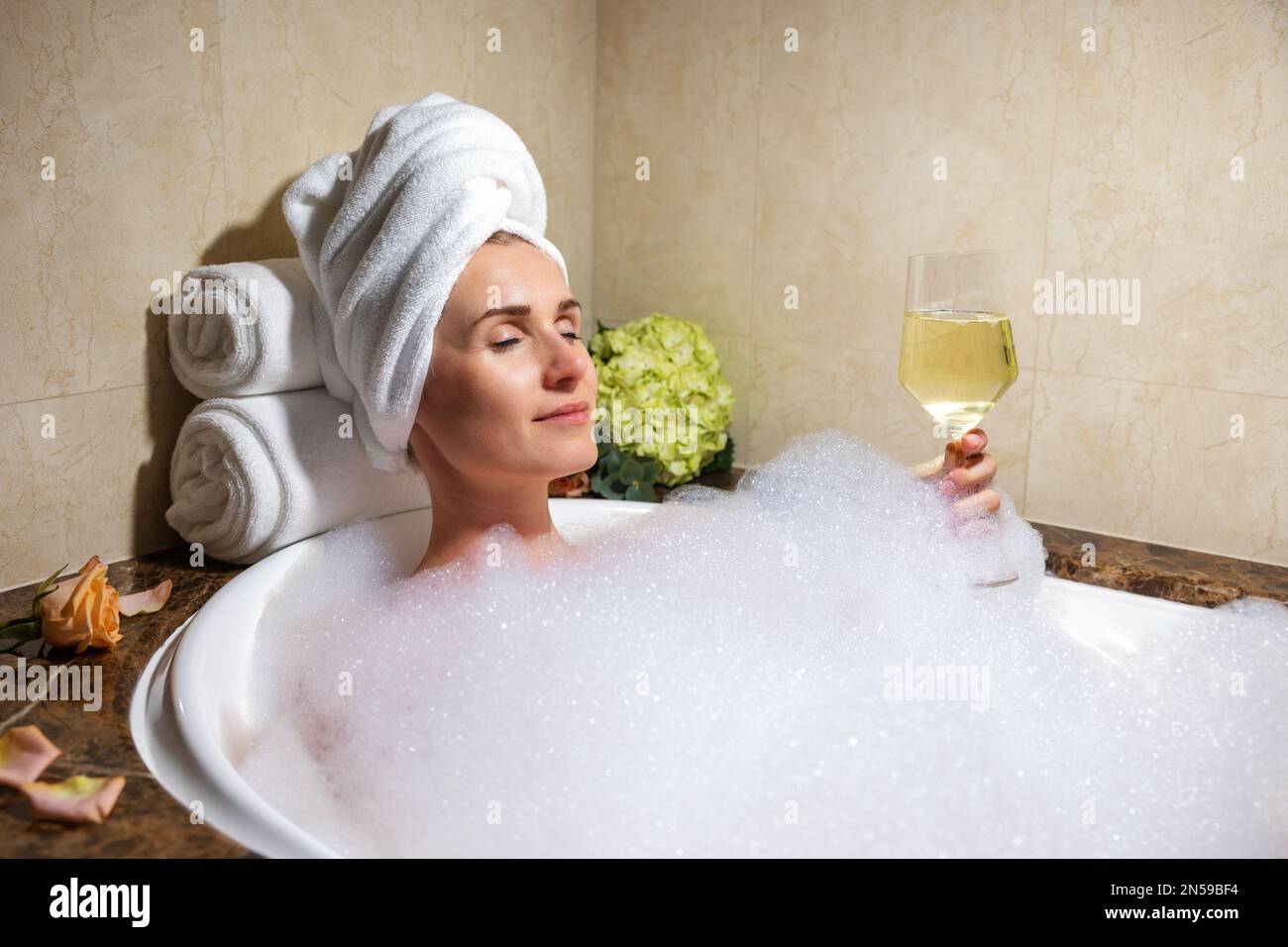 Donna che si rilassa in un bagno pieno di schiuma con un bicchiere di champagne nell'hotel SPA Foto Stock