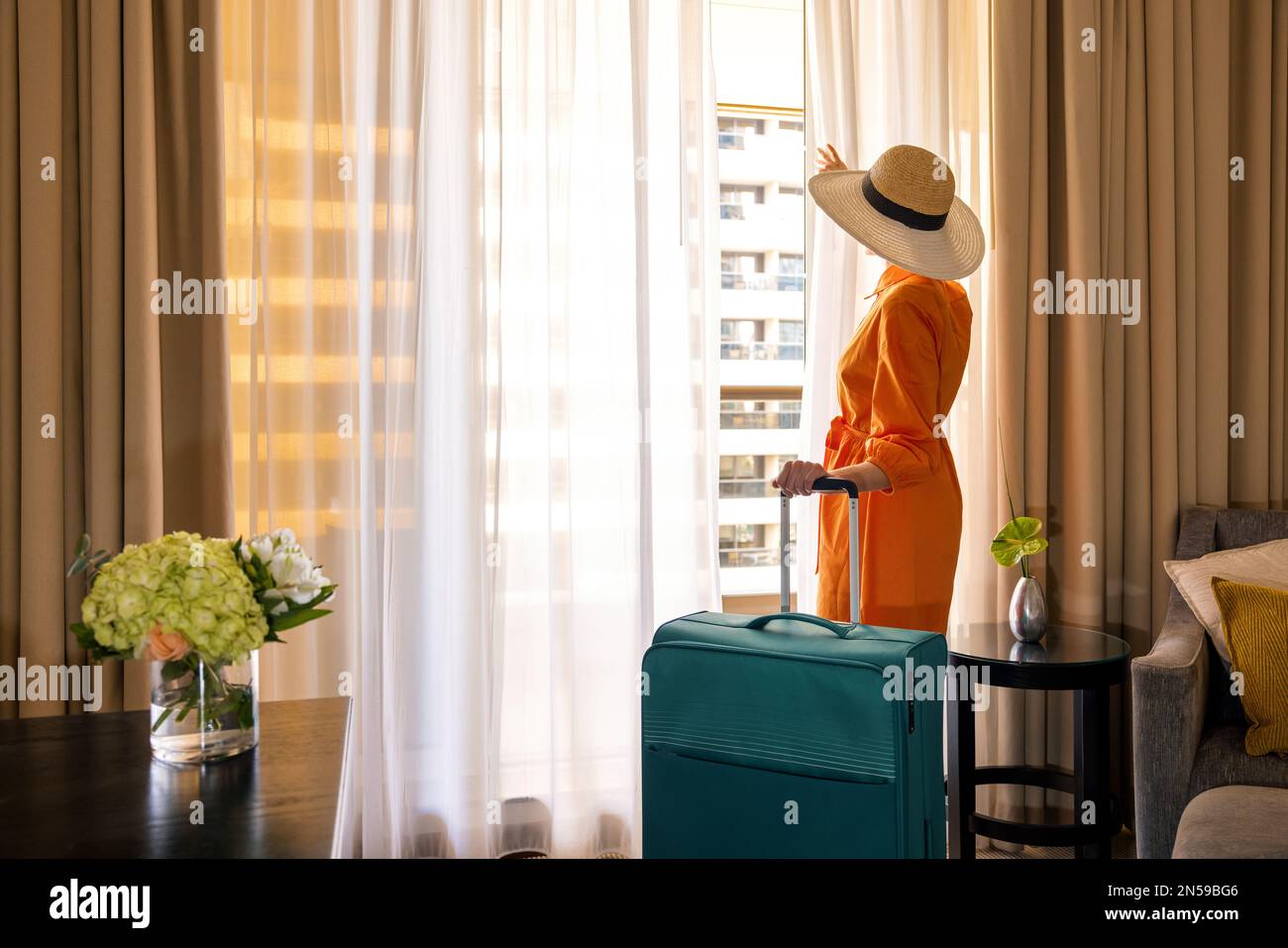 donna singola con bagagli che guarda fuori dalla finestra della camera dopo l'arrivo al resort Foto Stock